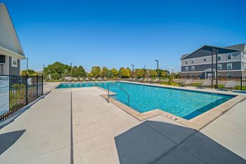 A large swimming pool surrounded by a concrete deck and a black fence.